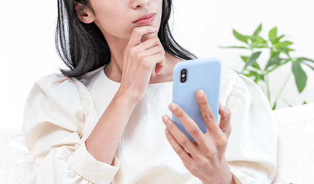 スマートフォンを見ながら考え込む女性