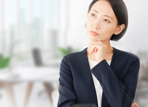 顎に手を当てて考え事をするスーツ姿の女性
